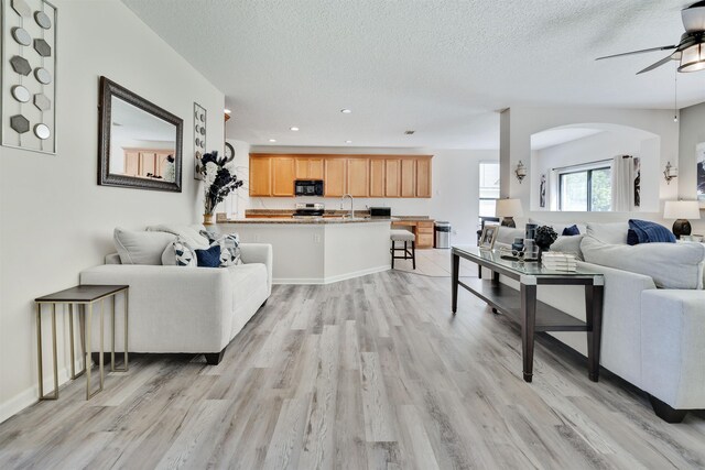 living room featuring ceiling fan, sink, a textured ceiling, and light hardwood / wood-style flooring