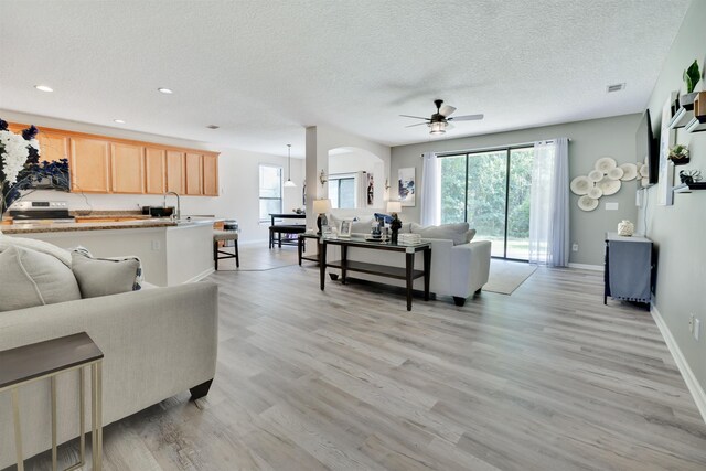 living room with ceiling fan, light hardwood / wood-style floors, and a textured ceiling