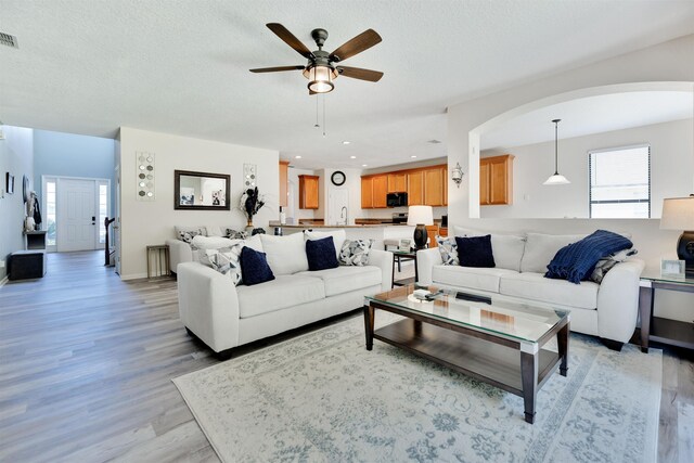 living room with ceiling fan, sink, a textured ceiling, and light wood-type flooring