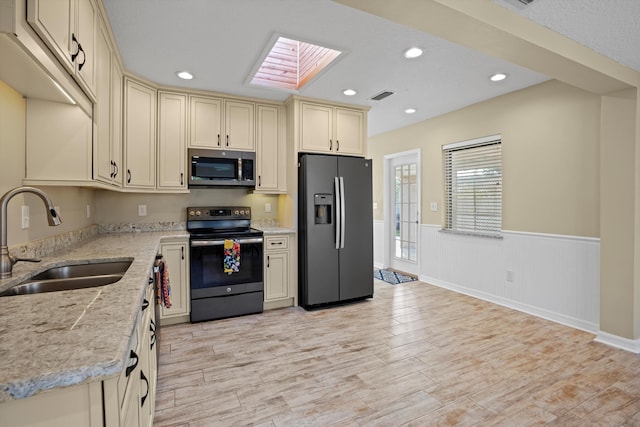 kitchen featuring a skylight, light stone countertops, sink, cream cabinetry, and appliances with stainless steel finishes