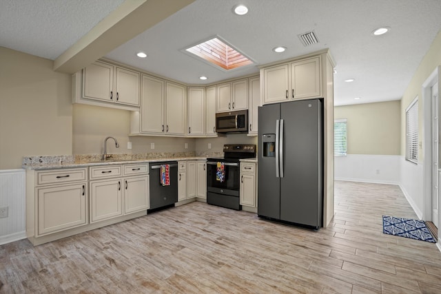 kitchen with a skylight, sink, light stone counters, light hardwood / wood-style floors, and appliances with stainless steel finishes