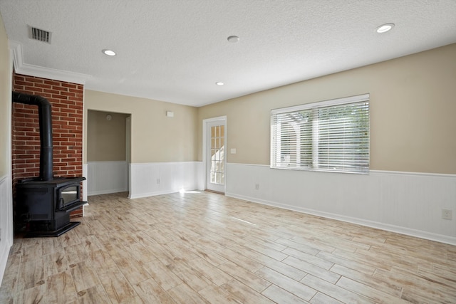 unfurnished living room featuring light wood-type flooring, a textured ceiling, and a wood stove