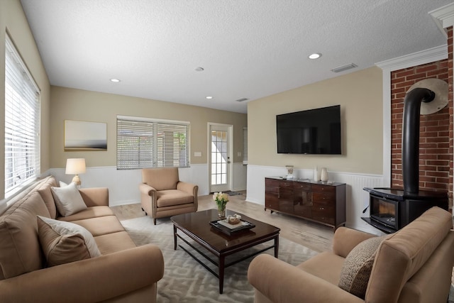 living room featuring a textured ceiling, light wood-type flooring, a wood stove, and a healthy amount of sunlight