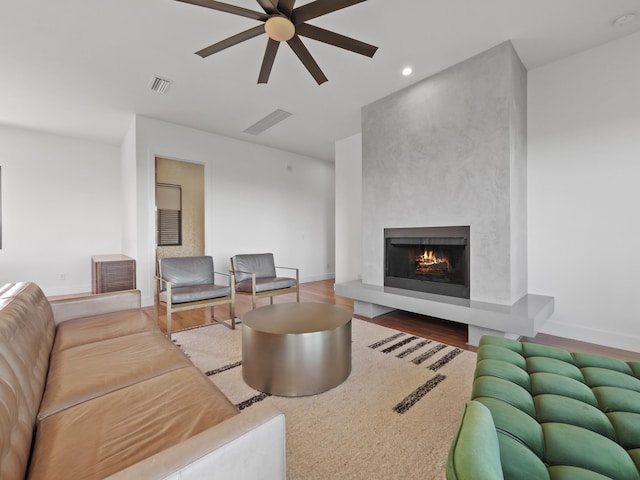 living room with hardwood / wood-style floors, ceiling fan, and a large fireplace