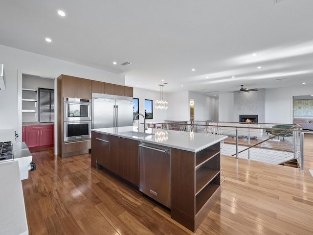 kitchen with sink, decorative light fixtures, a kitchen island with sink, a fireplace, and appliances with stainless steel finishes