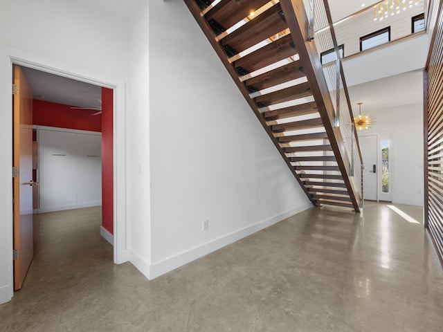 staircase with concrete flooring, a high ceiling, and an inviting chandelier