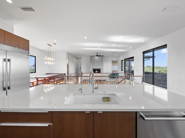 kitchen featuring a kitchen island with sink, sink, decorative light fixtures, a large fireplace, and stainless steel appliances