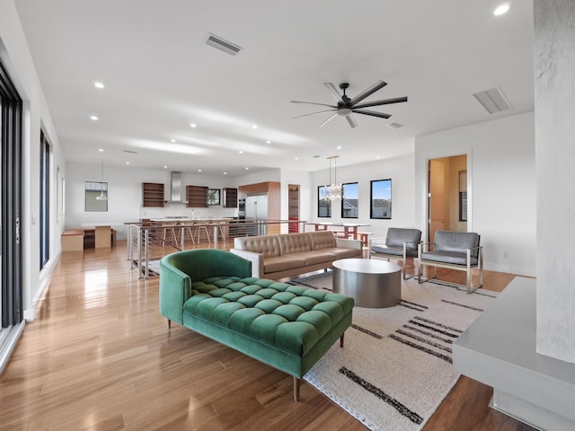 living room featuring ceiling fan with notable chandelier and light wood-type flooring