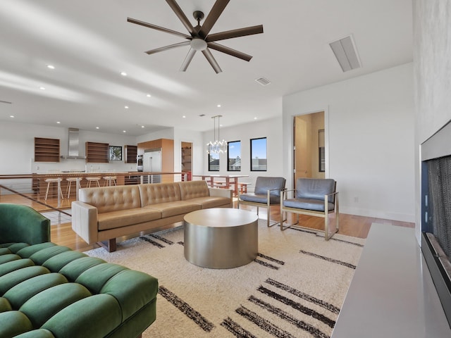 living room with ceiling fan with notable chandelier and light hardwood / wood-style floors