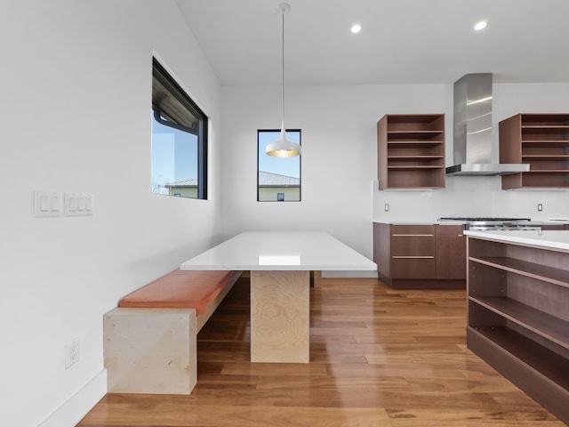 kitchen featuring wall chimney exhaust hood, pendant lighting, a breakfast bar area, a kitchen island, and light wood-type flooring