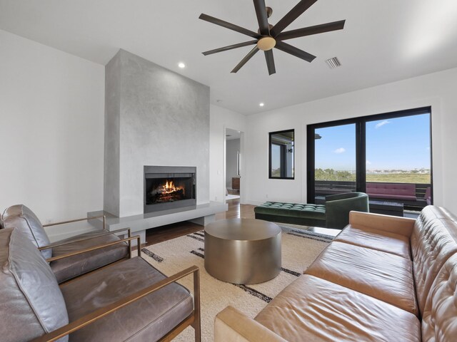 living room with ceiling fan, a large fireplace, and hardwood / wood-style floors