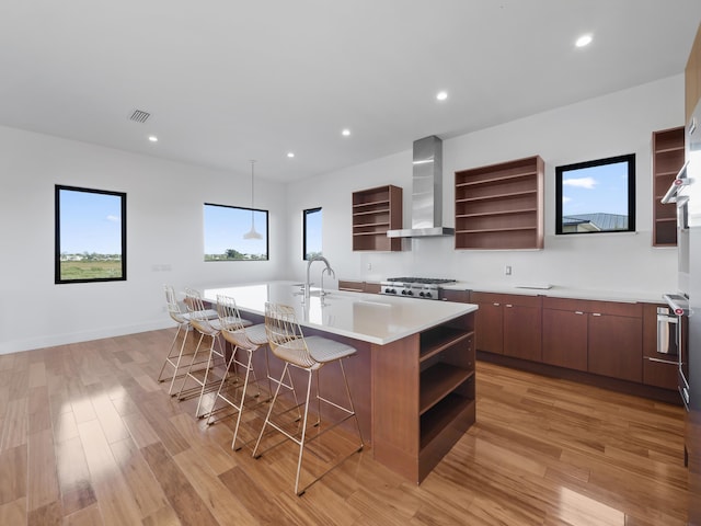 kitchen with stove, wall chimney exhaust hood, a large island with sink, light hardwood / wood-style flooring, and a breakfast bar area