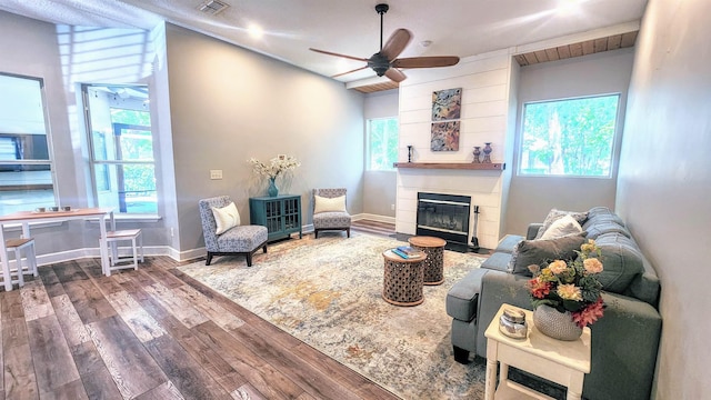living area with hardwood / wood-style flooring, a glass covered fireplace, ceiling fan, and baseboards