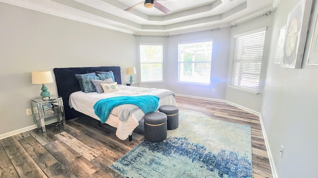 bedroom featuring wood finished floors, baseboards, a raised ceiling, ornamental molding, and a ceiling fan
