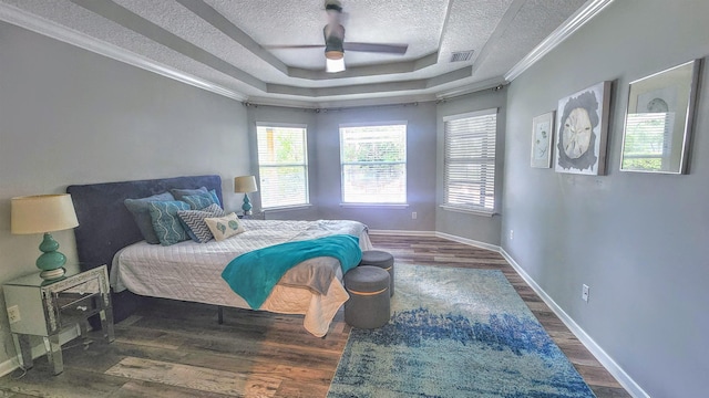 bedroom with a tray ceiling, a textured ceiling, wood finished floors, baseboards, and ornamental molding