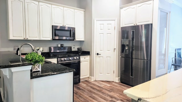 kitchen featuring appliances with stainless steel finishes, a peninsula, wood finished floors, white cabinets, and a sink