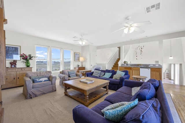 living room featuring visible vents, light wood-style floors, ceiling fan, and stairway