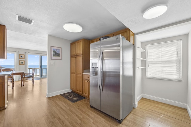 kitchen with brown cabinetry, visible vents, light wood-style floors, a textured ceiling, and stainless steel fridge