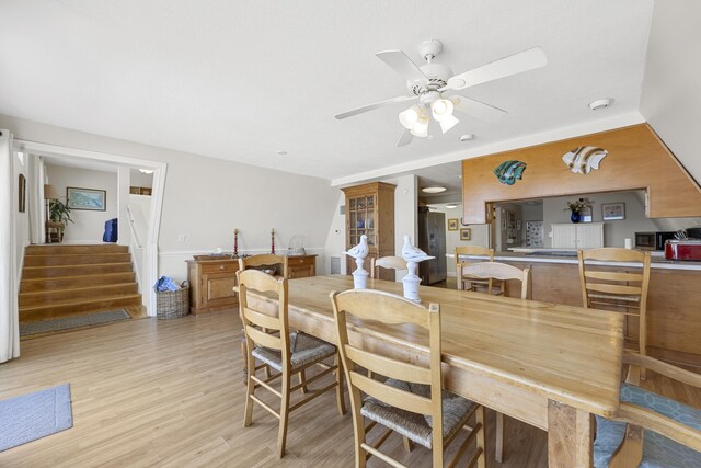 dining space featuring stairway, light wood-type flooring, and a ceiling fan