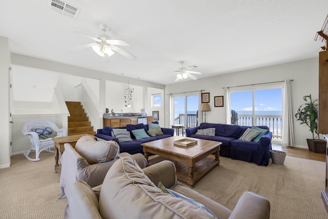 living room with visible vents, baseboards, a ceiling fan, and stairs