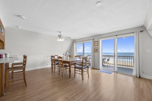 dining room with a textured ceiling, baseboards, light wood finished floors, and ceiling fan