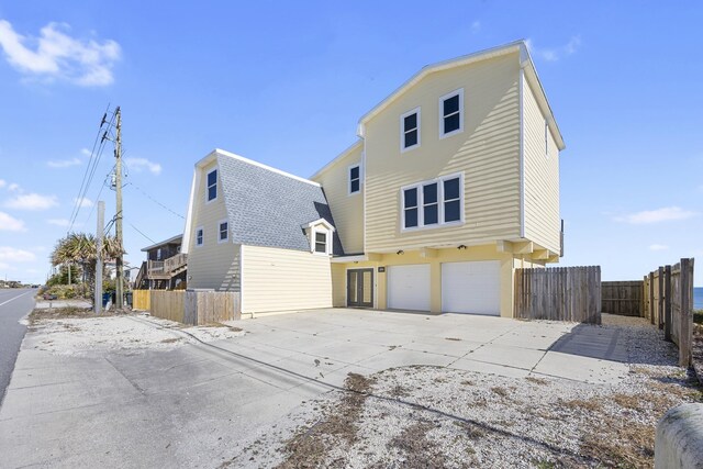 rear view of house featuring an attached garage, concrete driveway, roof with shingles, and fence