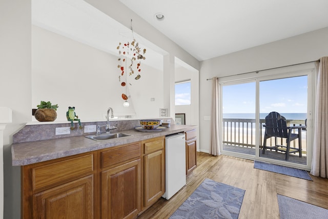 kitchen featuring light wood finished floors, a water view, dishwasher, brown cabinetry, and a sink