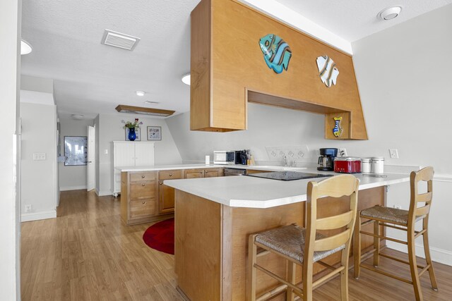 kitchen with a peninsula, light countertops, visible vents, and light wood finished floors