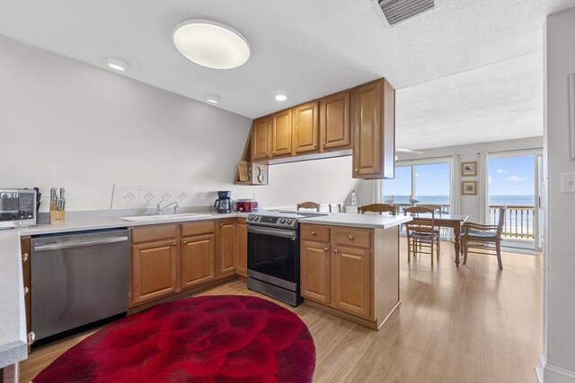 kitchen featuring visible vents, a sink, appliances with stainless steel finishes, a peninsula, and light wood finished floors