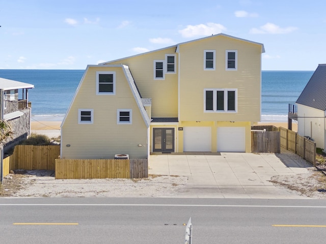 view of front of property featuring a water view, driveway, fence, french doors, and a garage