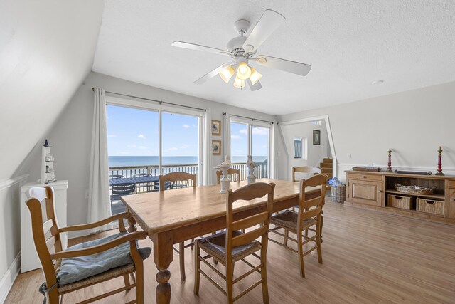 dining room featuring a water view, a textured ceiling, light wood-style flooring, and a ceiling fan