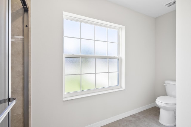 bathroom with toilet, plenty of natural light, a shower with door, and tile patterned flooring