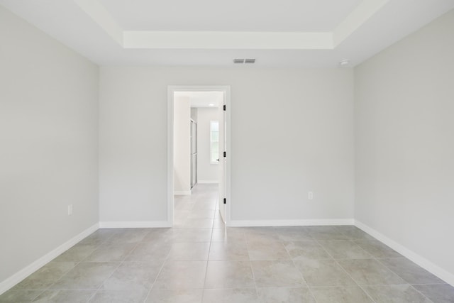 tiled empty room featuring a raised ceiling