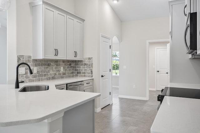 kitchen with kitchen peninsula, appliances with stainless steel finishes, decorative backsplash, sink, and light tile patterned floors