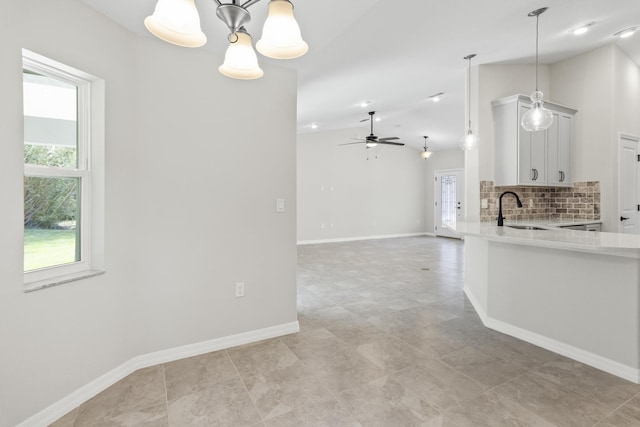 kitchen with lofted ceiling, backsplash, white cabinets, sink, and hanging light fixtures