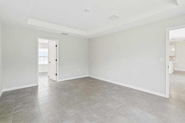 empty room featuring a raised ceiling and light tile patterned flooring