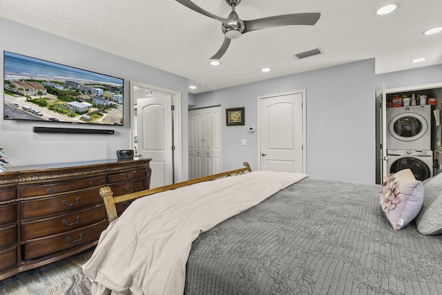 bedroom featuring two closets, ceiling fan, stacked washing maching and dryer, and a textured ceiling