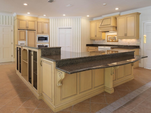 kitchen with stainless steel microwave, dark stone countertops, a spacious island, a kitchen bar, and custom range hood