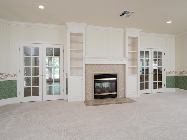 unfurnished living room with a tile fireplace, french doors, light colored carpet, and built in features