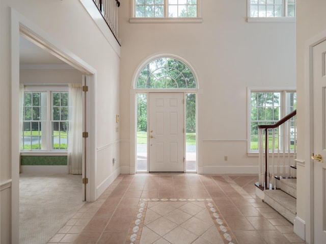 carpeted foyer with crown molding, plenty of natural light, and a high ceiling