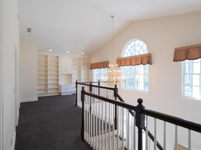 hallway featuring a notable chandelier, dark carpet, built in features, and vaulted ceiling