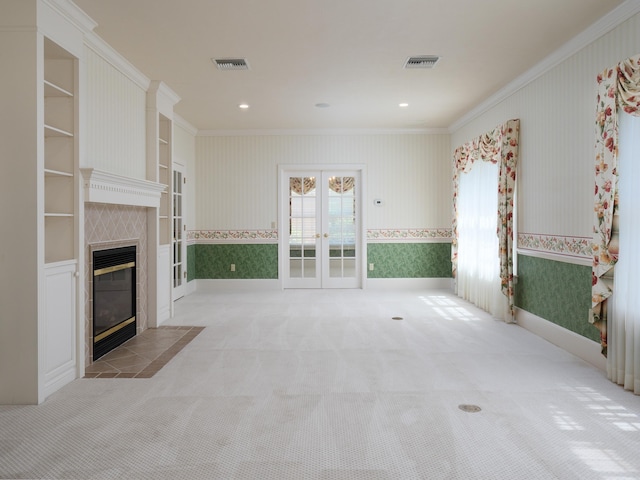 unfurnished living room featuring a tile fireplace, french doors, light colored carpet, and ornamental molding