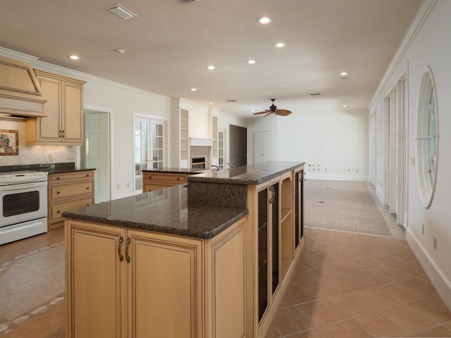 kitchen with tasteful backsplash, dark stone countertops, an island with sink, white range with electric cooktop, and light tile patterned flooring