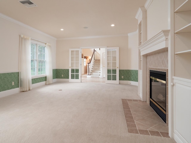 unfurnished living room featuring a tile fireplace, light carpet, french doors, and ornamental molding