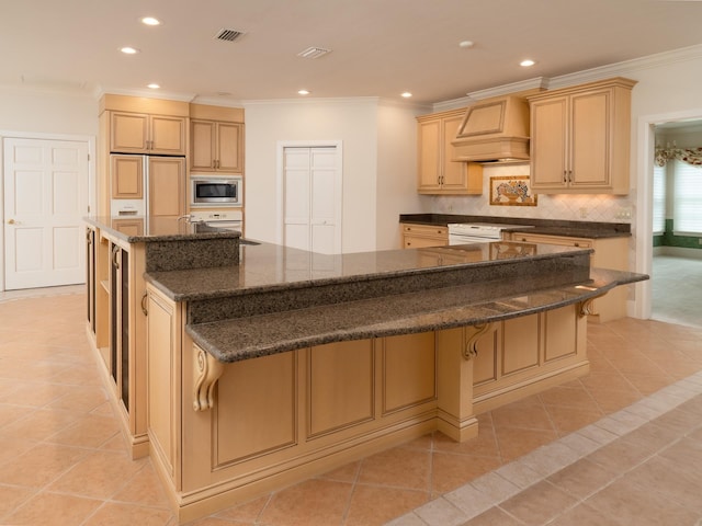 kitchen featuring a breakfast bar, custom range hood, stainless steel microwave, and a spacious island