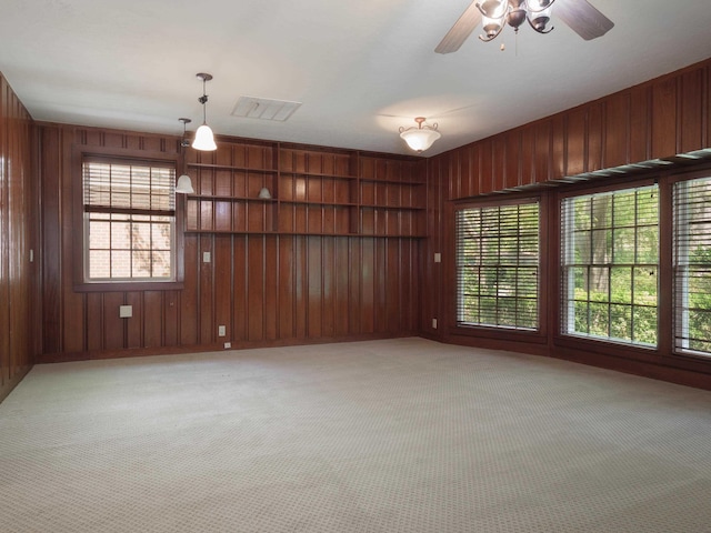 carpeted empty room with ceiling fan and wooden walls