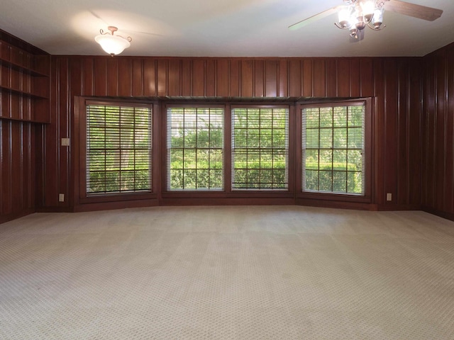 spare room with light carpet, ceiling fan, and wood walls