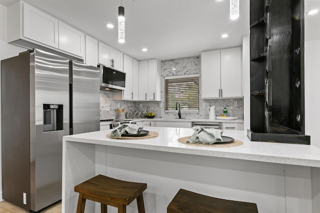 kitchen with white cabinets, a kitchen breakfast bar, hanging light fixtures, and appliances with stainless steel finishes