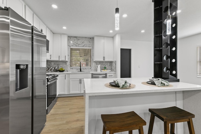 kitchen featuring white cabinets, pendant lighting, a kitchen bar, and stainless steel appliances