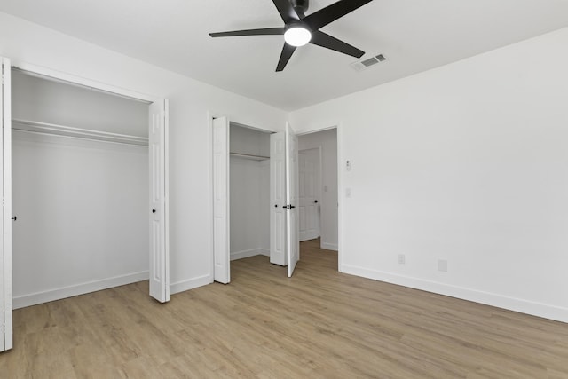 unfurnished bedroom featuring ceiling fan, light wood-type flooring, and two closets